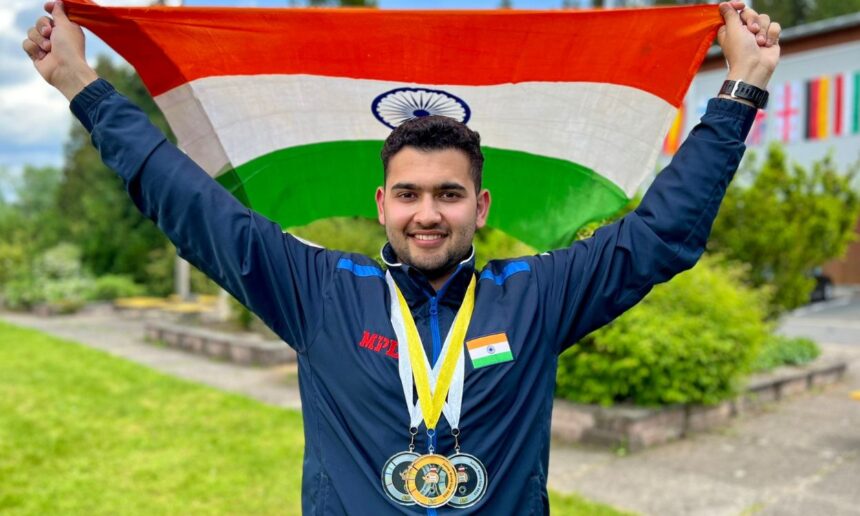 An image of Anish Bhanwala wearing 3 medals and holding the Indian Flag above his head