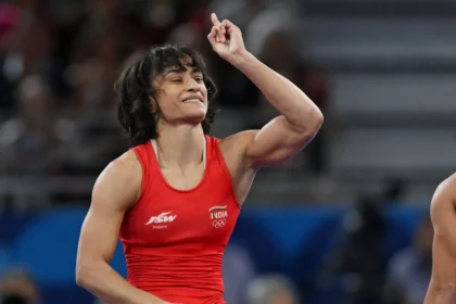 A photo of Vinesh Phogat wearing a red jersey and raising her left hand.