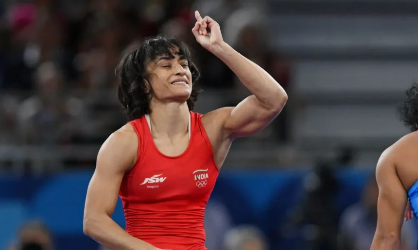 A photo of Vinesh Phogat wearing a red jersey and raising her left hand.